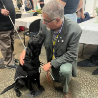 Kevin Prince kneeling next to Kevin the black lab guide dog