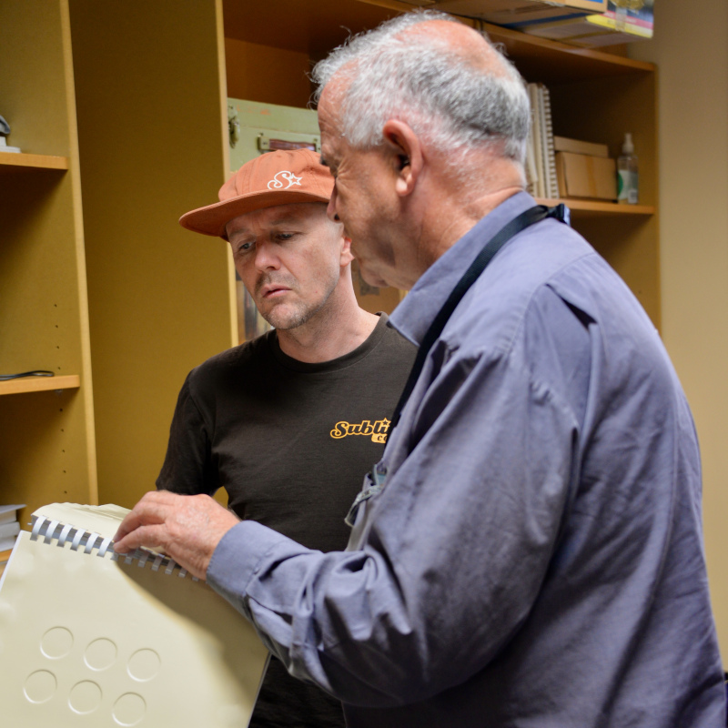 Peter reading Braille using touch, showing a colleague how to learn the basics