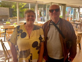 Chandra standing next to Neil Jarvis in a cafe. Both of them are smiling for the camera