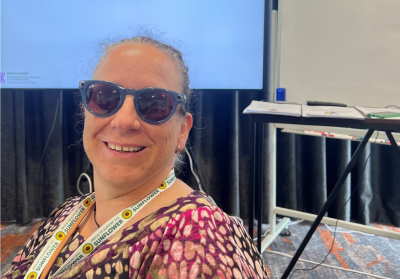 Sally Britnell wearing her Meta Glasses. Sally is sitting in a conference room and she is smiling at the camera