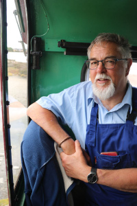 Kev smiling and leaning nonchalantly on his engine driver's chair, rocking his blue shirt and blue overalls.