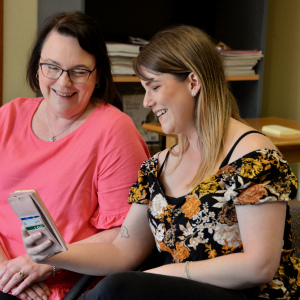 Katherine and Kirsten smiling over a shared moment on a mobile phone