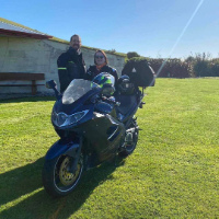 Katherine and her husband Gavin standing behind their blue Triump motorbike