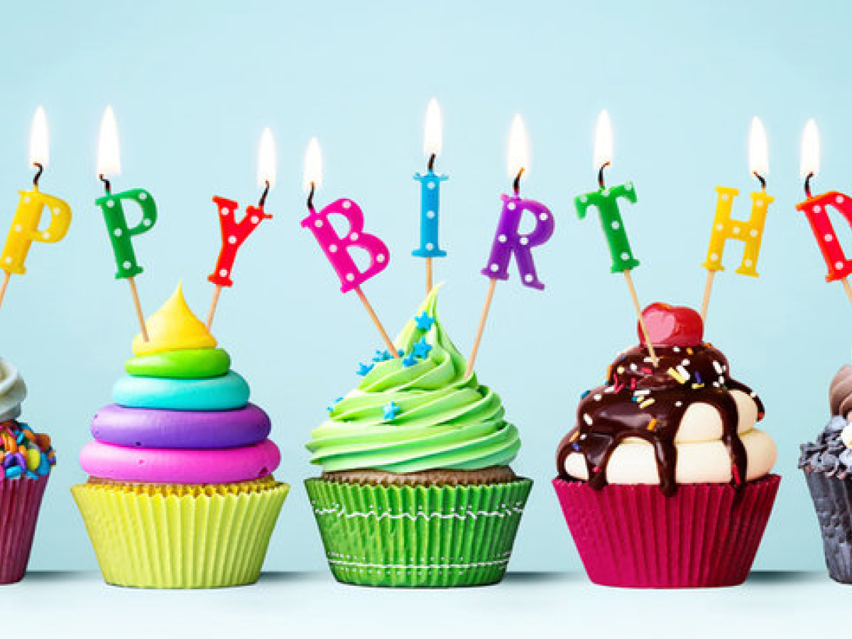 Colourful candles sticking out of brightly coloured iced cup cakes spelling Happy Birthday