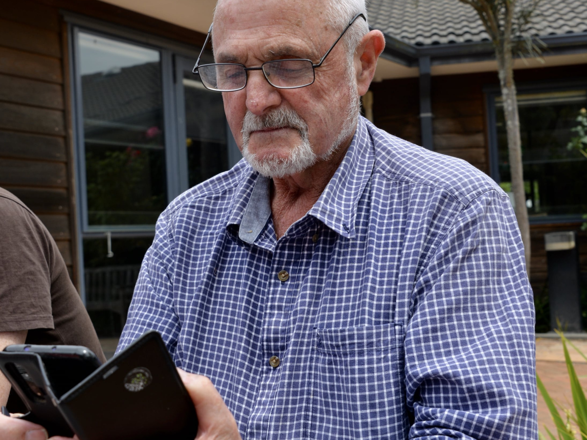 Older man with grey hair wearing a blue shirt sitting outside reading his phone
