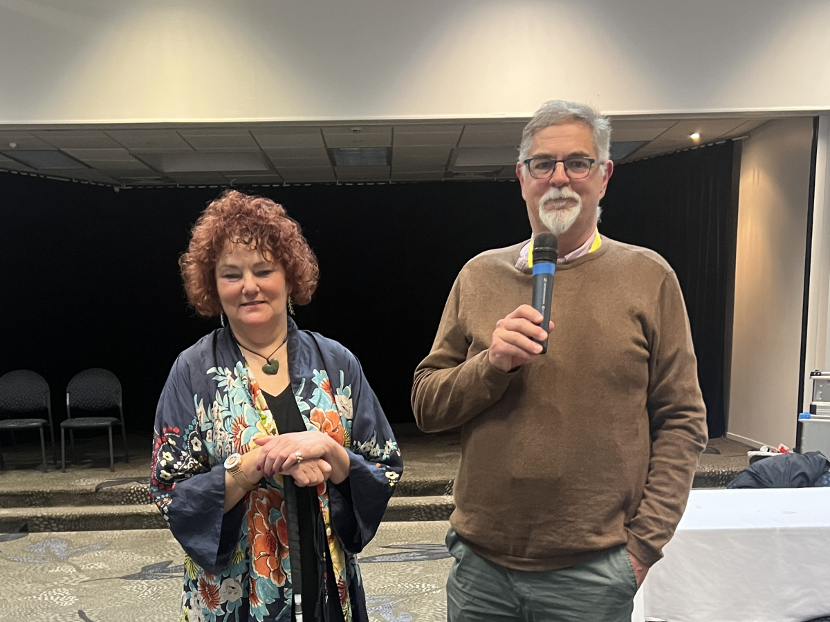 Amanda Stevens, chief executive, and Kevin Prince, President of the deafblind association of New Zealand standing to address the conference. Amanda is holding her Kevin is holding microphone