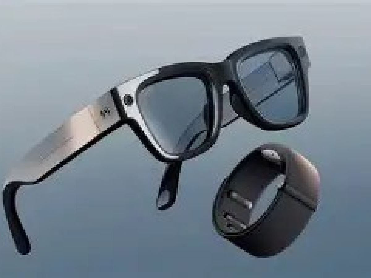 An open pair of black Meta Glasses in the classic Ray-Ban style with a camera imbedded in the glass surround, displayed on top of a black smart ring. 
